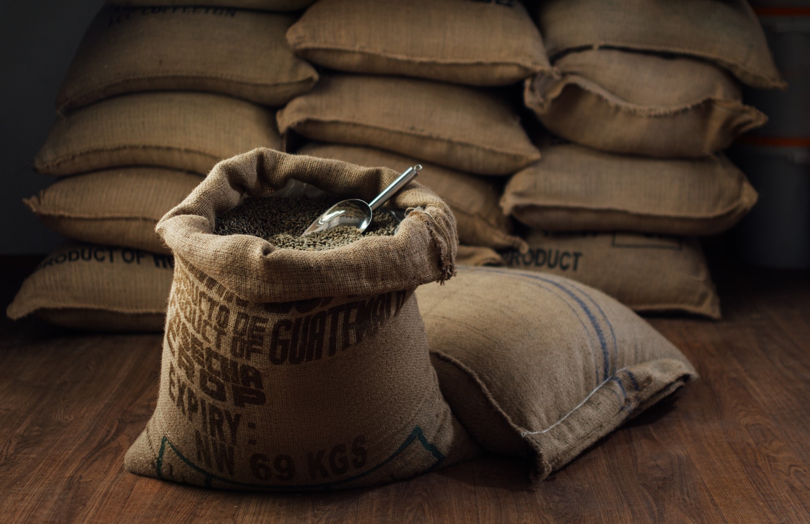open bag full of raw coffee beans with a metal scoop, in the background of the warehouse